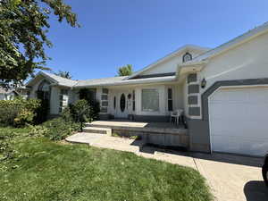 View of exterior entry with an attached garage, stucco siding, and a yard