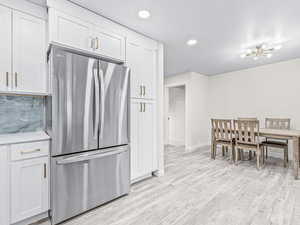 Kitchen with freestanding refrigerator, recessed lighting, light wood-style floors, white cabinets, and tasteful backsplash