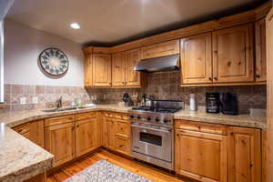 Kitchen featuring designer Wolf stove, light wood finished floors, backsplash, under cabinet range hood, and recessed lighting
