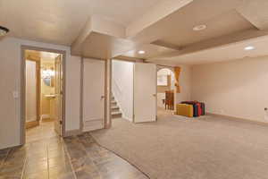 Finished below grade area with light colored carpet, light tile patterned flooring, stairs, and recessed lighting