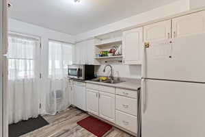 Kitchen featuring white appliances, open shelves, light wood-style floors, and white cabinetry