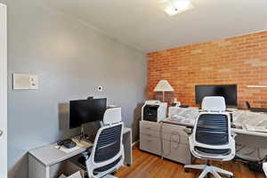 Office featuring wood finished floors, brick wall, and an accent wall