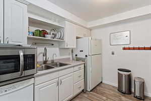 Kitchen featuring white appliances, light wood-style flooring, light countertops, open shelves, and white cabinets