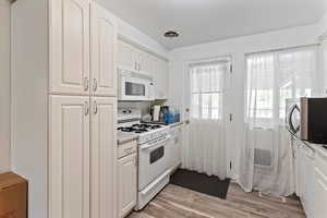 Kitchen featuring white appliances, white cabinets, light wood finished floors, and light countertops