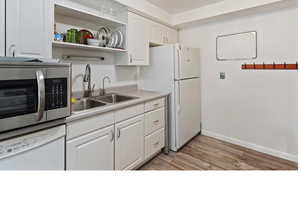 Kitchen featuring stainless steel microwave, white dishwasher, light countertops, open shelves, and light wood-type flooring