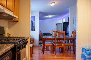Kitchen with black range with gas stovetop, light wood-type flooring, under cabinet range hood, and a textured ceiling