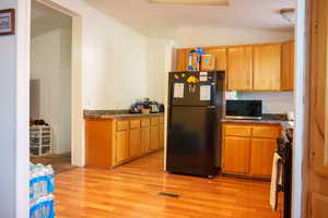 Kitchen featuring light wood-type flooring, black appliances, lofted ceiling, brown cabinets, and dark countertops