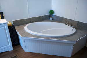 Full bath featuring a garden tub, dark wood-style floors, and vanity