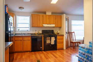 Kitchen with black appliances, ornamental molding, light wood-type flooring, under cabinet range hood, and brown cabinets