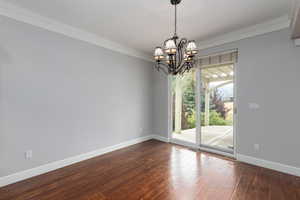 Unfurnished dining area with crown molding, dark wood-style floors, and a chandelier