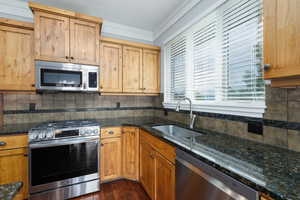 Kitchen with appliances with stainless steel finishes, decorative backsplash, dark stone counters, and dark wood-style floors