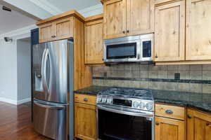Kitchen with appliances with stainless steel finishes, decorative backsplash, dark stone countertops, and dark wood-style floors