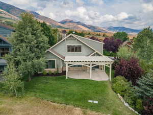 Back of house featuring stone siding, a mountain view, a yard, and a patio