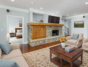 Living area featuring recessed lighting, wood finished floors, a fireplace, stairs, and crown molding