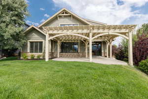 Rear view of house featuring a pergola, a lawn, a patio, and stone siding
