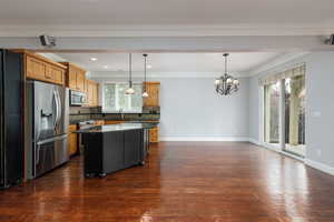 Kitchen with dark stone counters, appliances with stainless steel finishes, tasteful backsplash, a kitchen island, and pendant lighting