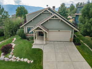 Craftsman-style house with stone siding, a front yard, concrete driveway, and a mountain view