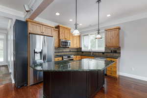 Kitchen featuring dark stone counters, decorative backsplash, stainless steel appliances, pendant lighting, and a center island