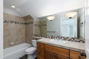 Full bath with tasteful backsplash, vanity, bathing tub / shower combination, lofted ceiling, and dark tile patterned flooring
