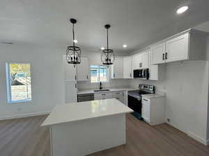 Kitchen with appliances with stainless steel finishes, light wood-type flooring, white cabinets, a center island, and pendant lighting