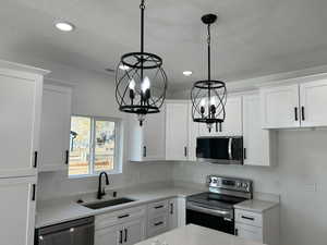 Kitchen featuring appliances with stainless steel finishes, white cabinets, decorative light fixtures, light stone counters, and recessed lighting
