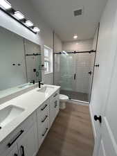 Full bathroom with double vanity, dark wood finished floors, a stall shower, and recessed lighting