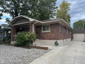 View of front of property with a detached garage, an outdoor structure, concrete driveway, and brick siding