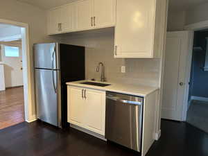 Kitchen featuring white cabinets, appliances with stainless steel finishes, decorative backsplash, and dark wood finished floors