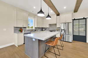 Kitchen with appliances with stainless steel finishes, white cabinetry, light wood-type flooring, a kitchen bar, and backsplash