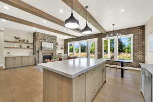 Kitchen featuring beamed ceiling, brick wall, a fireplace, decorative light fixtures, and light wood-style flooring