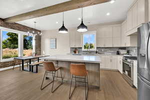 Kitchen with appliances with stainless steel finishes, decorative light fixtures, brick wall, light wood-type flooring, and a kitchen island