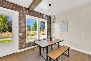 Dining area with brick wall, light wood-style floors, beamed ceiling, and a chandelier