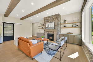 Living area with a barn door, light wood-style flooring, a fireplace, recessed lighting, and beam ceiling