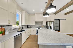 Kitchen featuring a barn door, stainless steel appliances, decorative backsplash, a kitchen island, and beamed ceiling
