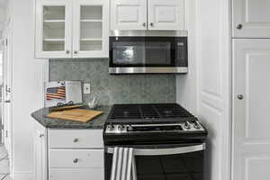 Kitchen with appliances with stainless steel finishes, tasteful backsplash, glass insert cabinets, and white cabinetry