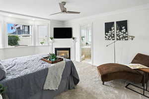 Bedroom featuring ornamental molding, ceiling fan, a lit fireplace, carpet flooring, and ensuite bathroom
