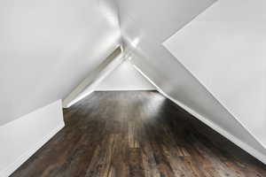 Bonus room with vaulted ceiling and dark wood-style flooring