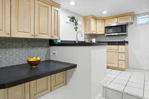 Kitchen with dark countertops, decorative backsplash, light tile patterned floors, light brown cabinetry, and recessed lighting