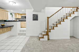 Kitchen featuring dark countertops, light tile patterned floors, stainless steel microwave, light brown cabinets, and recessed lighting