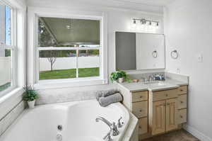 Full bath with vanity, a jetted tub, healthy amount of natural light, and crown molding
