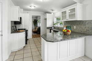 Kitchen featuring a peninsula, tasteful backsplash, light tile patterned floors, and white cabinetry