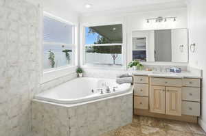 Bathroom featuring vanity, a whirlpool tub, crown molding, and light tile patterned floors