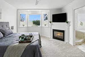 Bedroom with crown molding, carpet floors, connected bathroom, a ceiling fan, and a fireplace with flush hearth