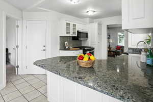 Kitchen with a peninsula, dark stone countertops, white cabinets, tasteful backsplash, and glass insert cabinets