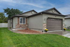 Ranch-style house with stone siding, an attached garage, stucco siding, and a front lawn