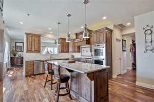 Kitchen featuring light stone counters, a kitchen bar, dark wood finished floors, a center island, and decorative light fixtures
