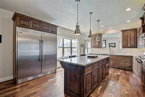 Kitchen featuring stainless steel appliances, light stone counters, dark wood finished floors, a center island, and decorative light fixtures
