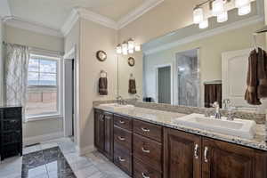 Bathroom with light marble finish flooring, crown molding, double vanity, and a shower stall