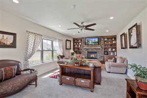 Carpeted living room featuring built in features, a stone fireplace, recessed lighting, and a ceiling fan