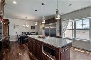 Kitchen featuring dark brown cabinetry, light stone countertops, built in appliances, a kitchen island, and decorative light fixtures